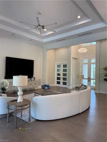 Living room with french doors, baseboards, a raised ceiling, and a ceiling fan