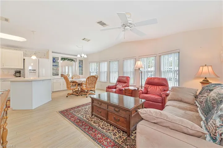 Living room featuring light wood-type flooring, ceiling fan with notable chandelier, and lofted ceiling