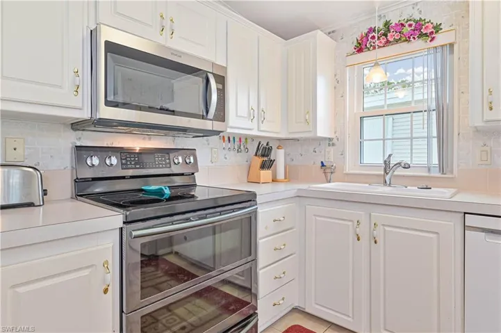 Kitchen featuring range with electric cooktop, dishwasher, sink, decorative backsplash, and white cabinetry