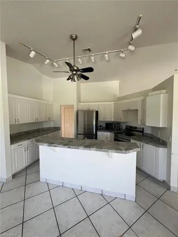 Kitchen featuring tile counters, track lighting, appliances with stainless steel finishes, ceiling fan, and light tile patterned floors