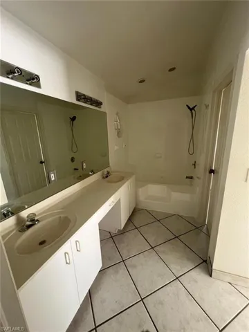 Bathroom with a tub to relax in, double vanity, light tile patterned flooring, and vaulted ceiling