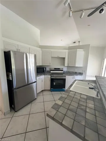 Kitchen with stainless steel appliances, tile counters, white cabinets, lofted ceiling, and rail lighting