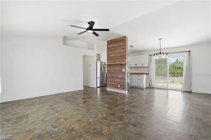 Open-concept living area featuring a modern black ceiling fan, stone-look tile flooring, and a partial wood-finish accent wall