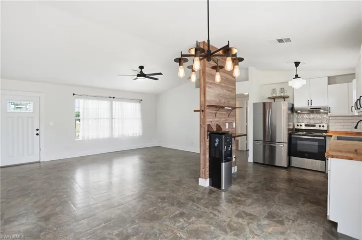 Open-concept living space featuring wood-finish flooring, a contemporary chandelier, and a decorative wood-paneled accent wall