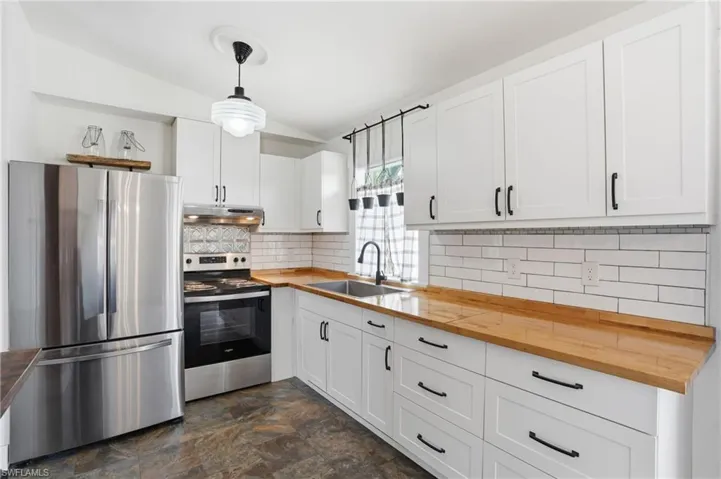 Kitchen featuring white shaker-style cabinetry, wood-finish countertops, stainless steel appliances, white subway tile backsplash, and slate-style flooring