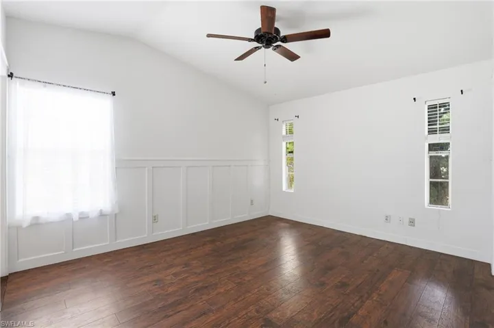Spacious room featuring wood-finish flooring, white board and batten wall detailing, and a vaulted ceiling with a ceiling fan