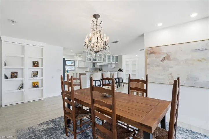 Bright dining area featuring an ornate chandelier, recessed lighting, and wood-finish flooring - Virtually Edited Image