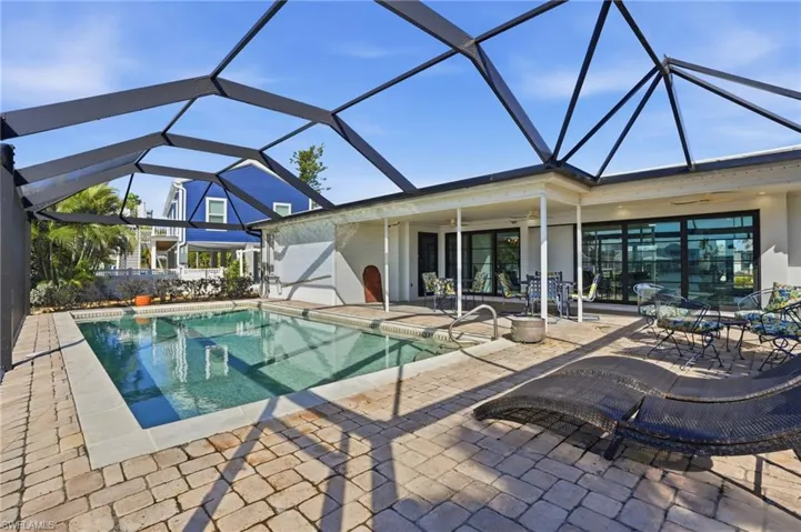 Screened swimming pool enclosure featuring a rectangular pool with integrated steps, a brick paver patio, and multiple large sliding glass doors providing access to the interior - Virtually Edited Image