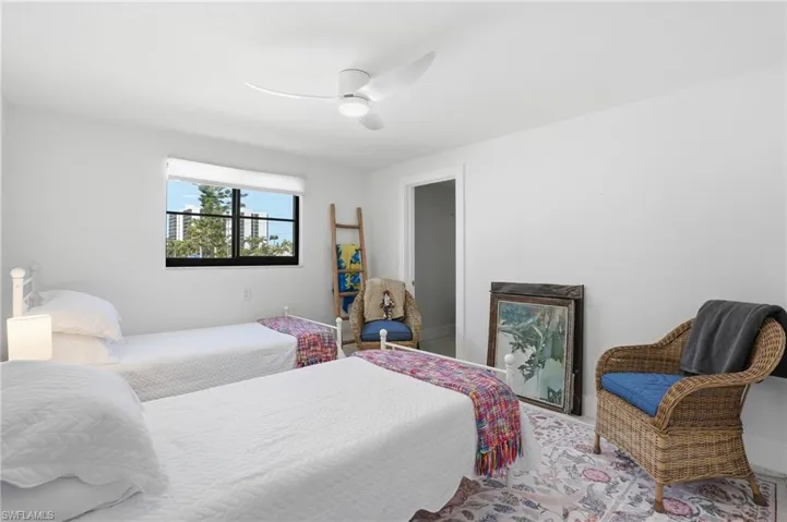 Bright bedroom featuring a single window with a roller shade, a contemporary ceiling fan, and light-colored walls - Virtually Edited Image