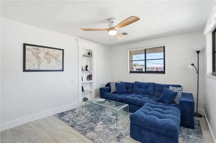 Living area featuring wood-finish flooring, a contemporary ceiling fan, and built-in shelving - Virtually Edited Image