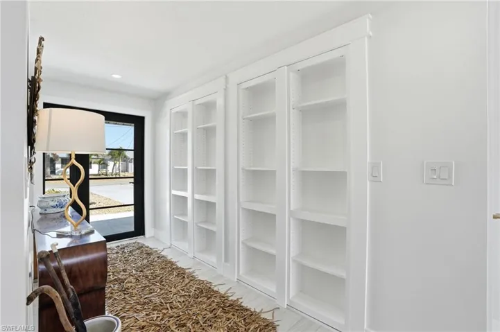 Entryway featuring a black-framed glass panel door, built-in white shelving, recessed lighting, and light-toned flooring - Virtually Edited Image