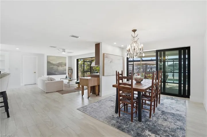 Open-concept living and dining areas featuring light wood-finish flooring, recessed lighting, and a crystal chandelier - Virtually Edited Image
