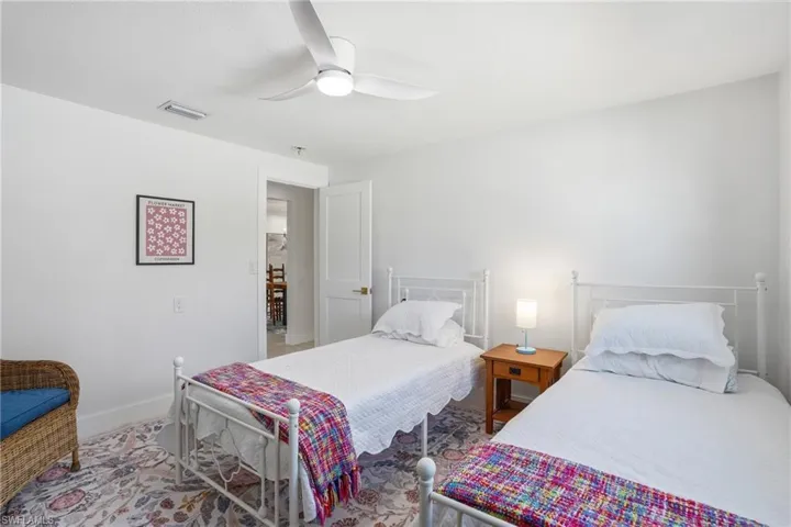 Bright room featuring a ceiling fan, white walls, a colorful patterned area rug, and a white door with brass hardware - Virtually Edited Image