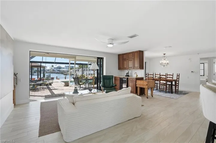 Open-concept living space featuring wood-finish flooring, a contemporary ceiling fan, and a wet bar with integrated beverage cooler - Virtually Edited Image
