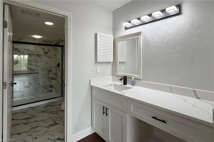 Full bath with vanity, a marble finish shower, dark marble finish floors, and recessed lighting