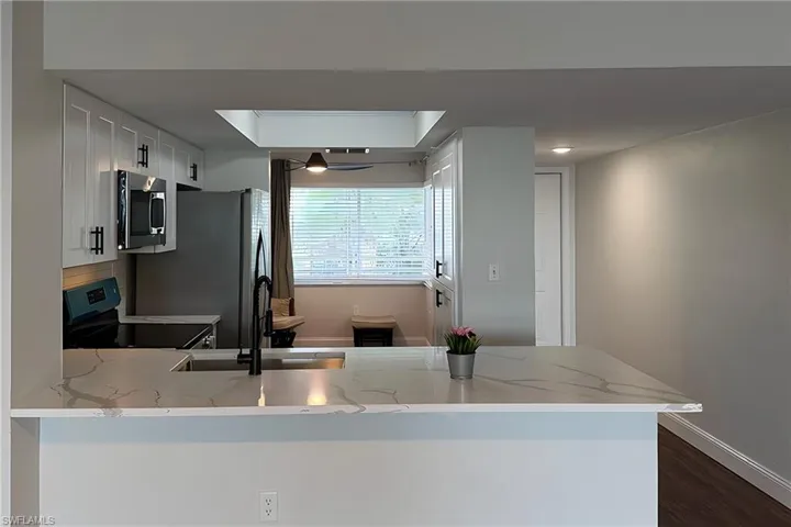 Kitchen featuring stainless steel appliances, light stone countertops, white cabinets, a peninsula, and dark wood finished floors