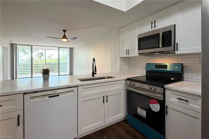 Kitchen with stainless steel appliances, white cabinets, dark wood-type flooring, decorative backsplash, and a peninsula