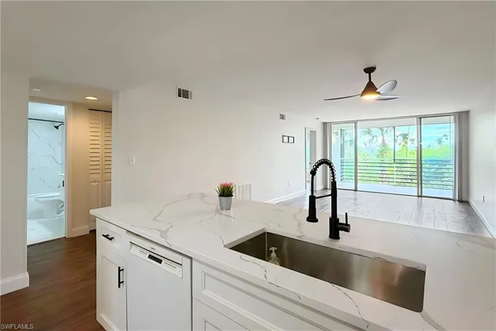 Kitchen featuring white dishwasher, white cabinets, light stone countertops, dark wood-type flooring, and open floor plan