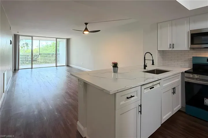 Kitchen with stainless steel appliances, expansive windows, a peninsula, white cabinets, and dark wood-style floors
