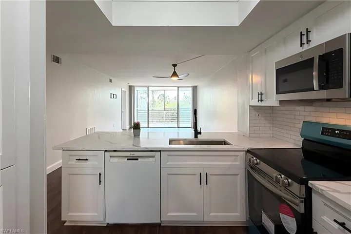 Kitchen featuring stainless steel appliances, white cabinetry, a peninsula, and dark wood-style flooring