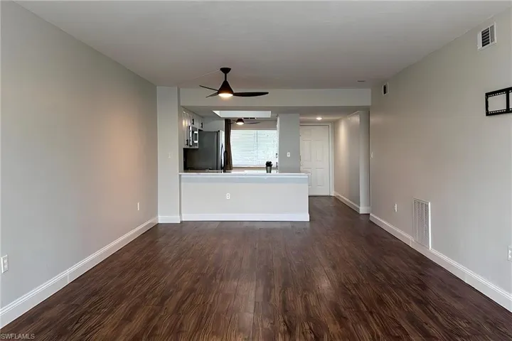 Unfurnished living room featuring a ceiling fan and dark wood-style flooring