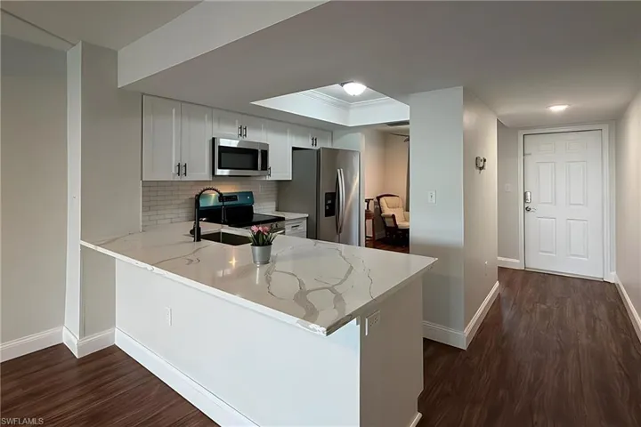 Kitchen featuring a peninsula, stainless steel appliances, dark wood-style floors, and white cabinets