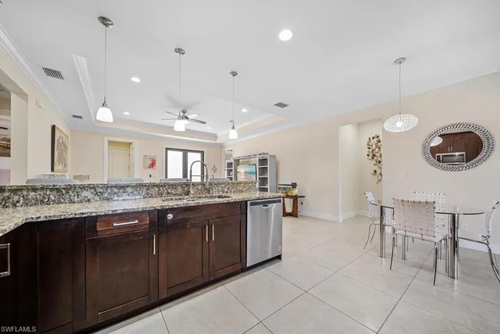 Kitchen with a ceiling fan, a sink, hanging light fixtures, dishwasher, and a raised ceiling