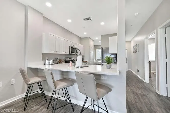 Kitchen with dark wood-type flooring, a kitchen bar, white cabinets, appliances with stainless steel finishes, and a peninsula