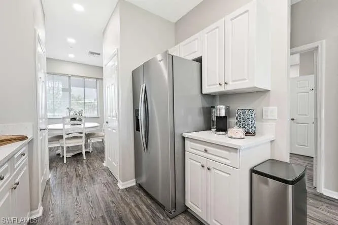 Kitchen with light countertops, white cabinets, dark wood-type flooring, stainless steel fridge, and recessed lighting