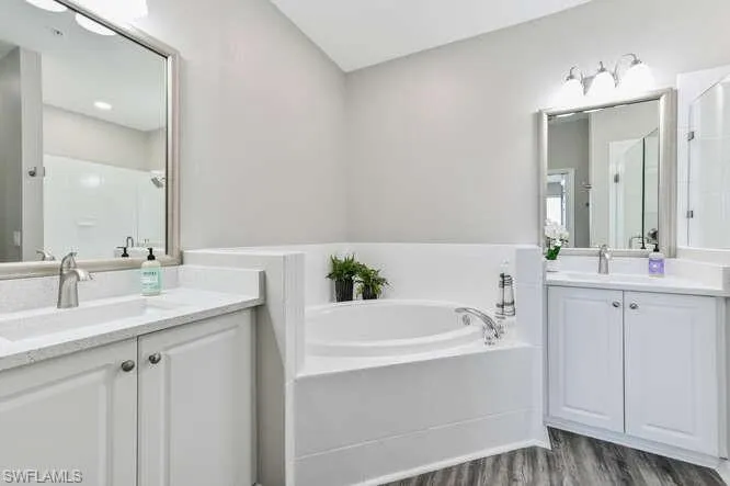 Bathroom with two vanities, a bath, a shower stall, and dark wood-style floors