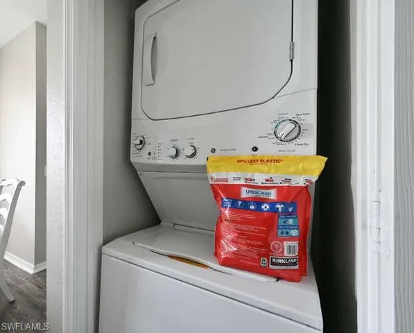 Laundry room with stacked washer and clothes dryer and dark wood-style flooring