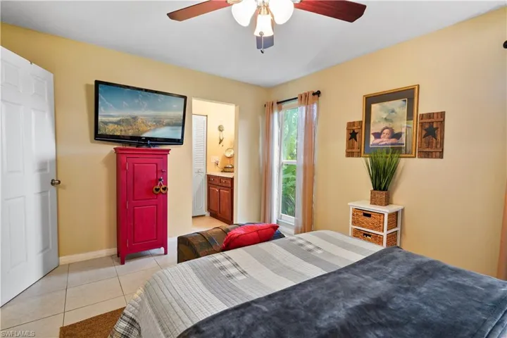 Bedroom with light tile patterned flooring, ensuite bathroom, and ceiling fan