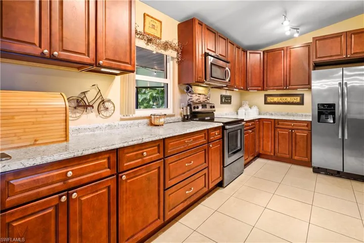 Kitchen with light tile patterned flooring, lofted ceiling, light stone like countertops, and appliances with stainless steel finishes