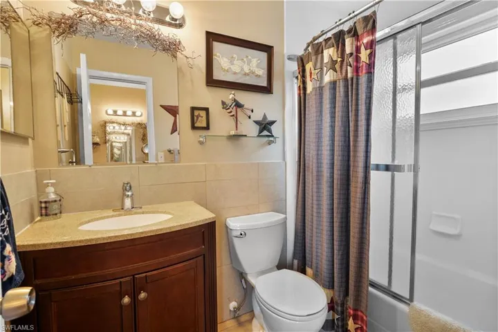 Full bathroom featuring tile walls, shower / bathtub combination with curtain, toilet, and vanity