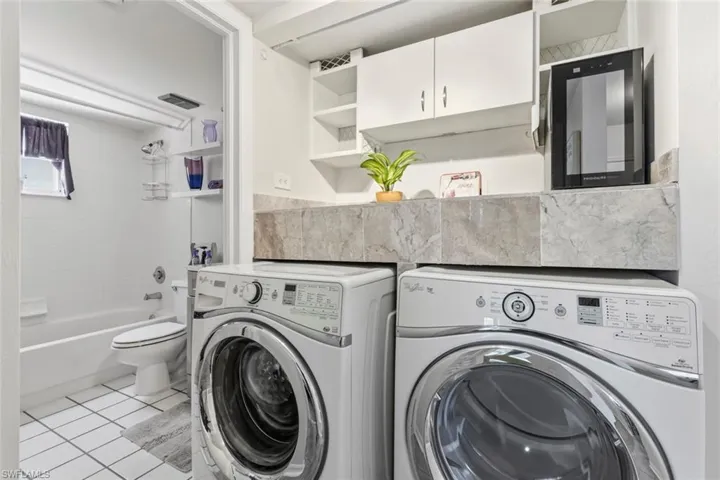 Combined utility and bathroom space featuring white subway tile walls, a built-in bathtub, and a window