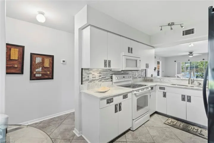 Bright kitchen featuring white cabinetry, light countertops, a tile backsplash, and a pass-through window
