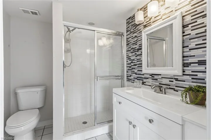 Bathroom featuring a glass-enclosed shower, white vanity with integrated sink, contemporary mosaic tile accent wall, framed mirror, and chrome fixtures