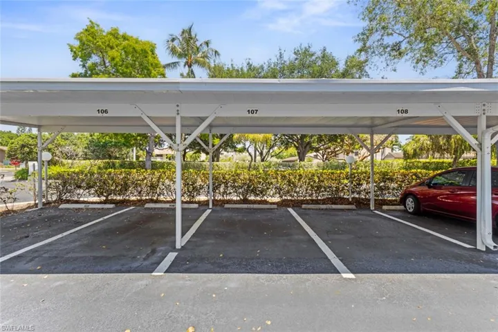 Assigned covered parking featuring numbered spaces, a white metal car port structure, and mature landscaping