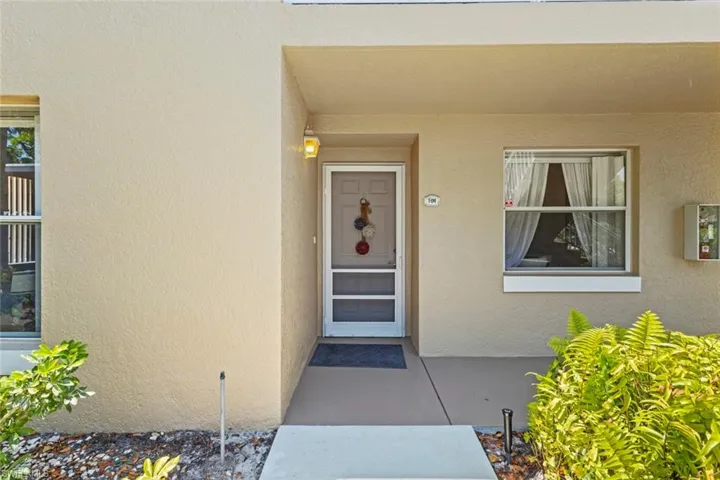 Warm beige stucco exterior with a covered entry, screened storm door, and decorative outdoor lighting fixture