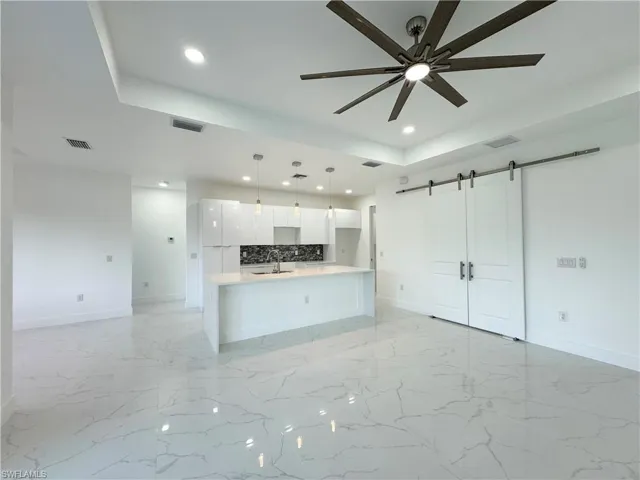 Unfurnished living room featuring a barn door, light tile flooring, and a raised ceiling