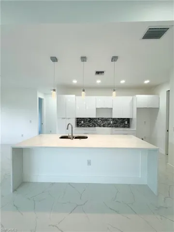 Kitchen with decorative light fixtures, light tile flooring, tasteful backsplash, a kitchen island with sink, and white cabinets