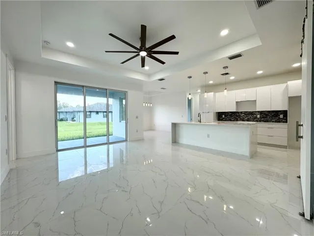 Kitchen with backsplash, a center island with sink, ceiling fan, and a tray ceiling