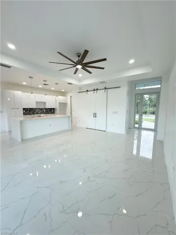 Unfurnished living room with a tray ceiling, a barn door, sink, ceiling fan, and light tile floors