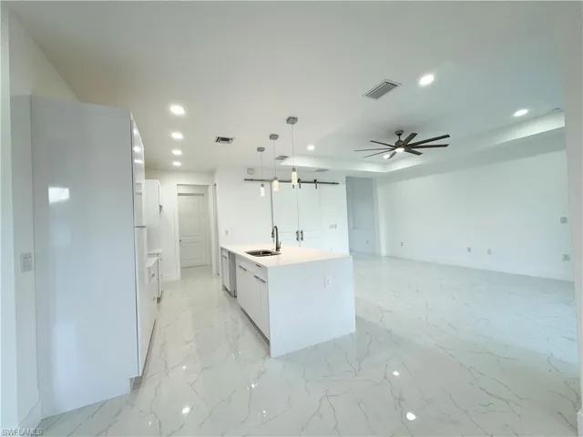Kitchen featuring ceiling fan, a center island with sink, decorative light fixtures, light tile floors, and sink
