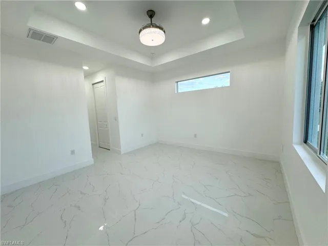 Spare room featuring a raised ceiling, a wealth of natural light, and light tile floors