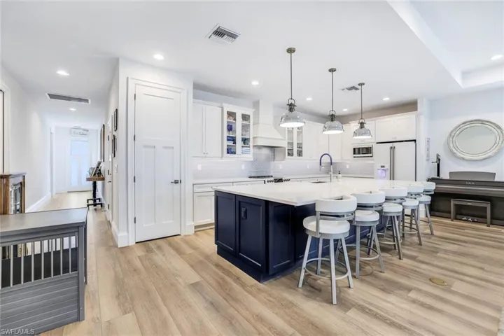 Kitchen featuring premium range hood, white cabinets, an island with sink, light wood-type flooring, and appliances with stainless steel finishes