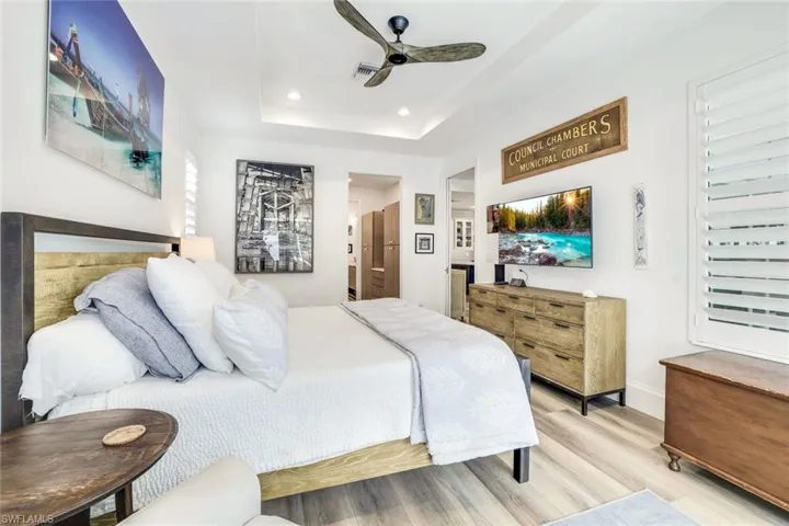 Bedroom featuring light hardwood / wood-style flooring, ensuite bathroom, ceiling fan, and a raised ceiling