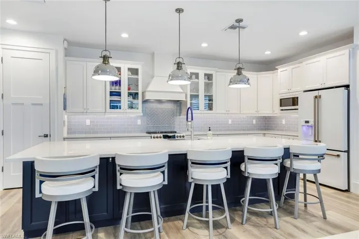 Kitchen with stainless steel microwave, light hardwood / wood-style flooring, tasteful backsplash, high end white refrigerator, and an island with sink