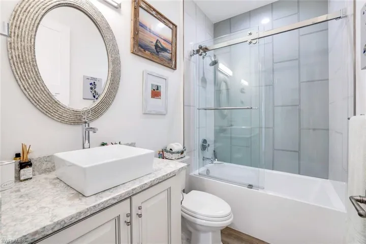 Full bathroom with hardwood / wood-style floors, bath / shower combo with glass door, toilet, and vanity