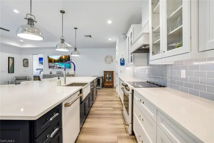 Kitchen featuring decorative light fixtures, decorative backsplash, white cabinets, white appliances, and light hardwood / wood-style flooring